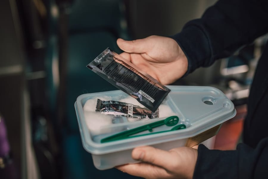 A pair of hands holding open a small travel first-aid kit containing foil-wrapped wipes, cotton wool and green tweezers.