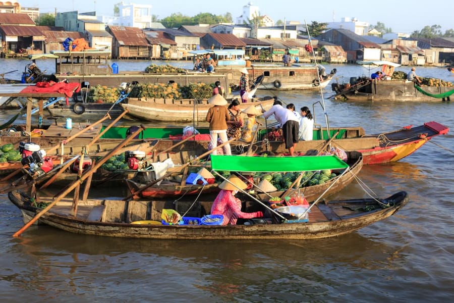 Vendors in conical hats sell produce from wooden boats piled with watermelons at a Mekong Delta floating market.