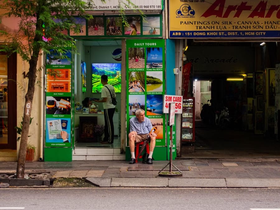A tour and SIM-card shopfront in Ho Chi Minh City, with a man seated on a stool outside beside a “SIM CARD 4G/5G” sign.