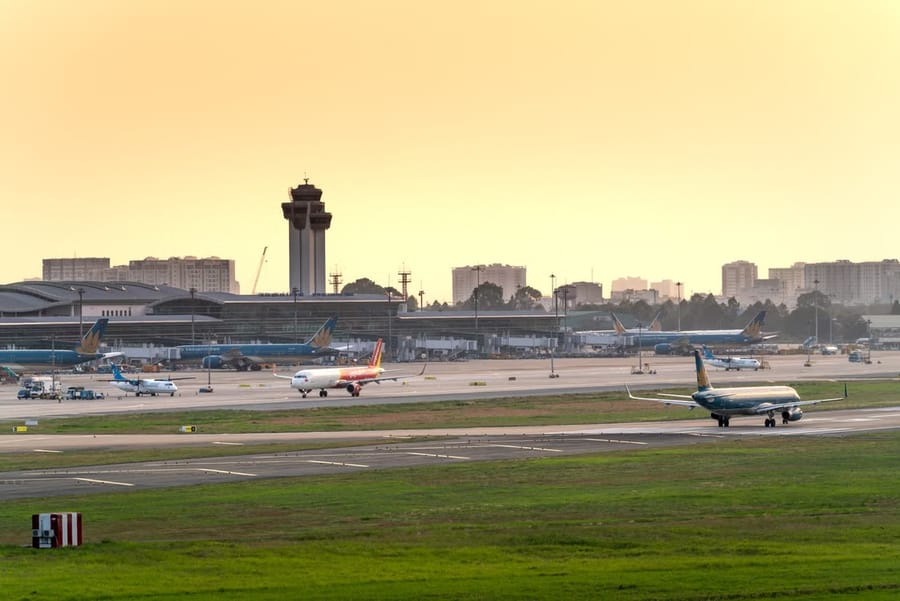 Planes from Vietnamese airlines taxi on the tarmac past the control tower at sunset.