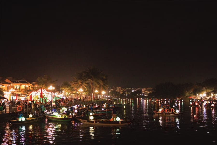 Lantern-lit boats crowd the Hoài River in Hội An at night, with festival lights glowing along the riverside promenade.
